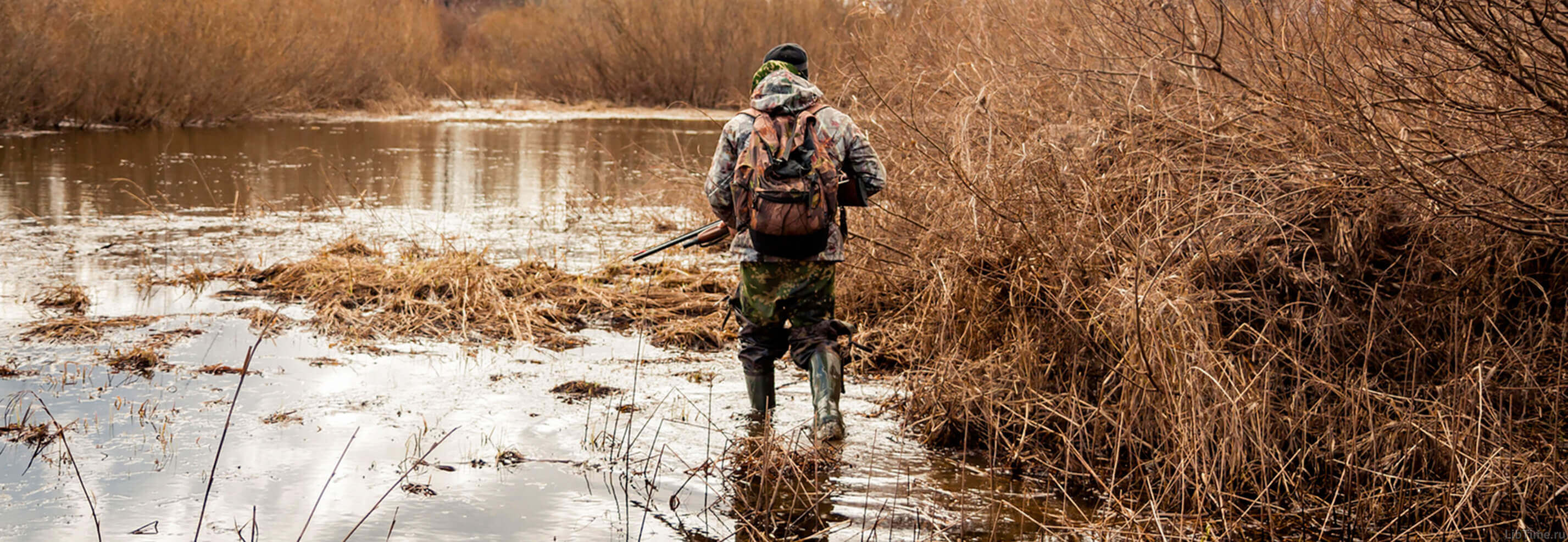 Hunter walking through a bog with a hunting rifle